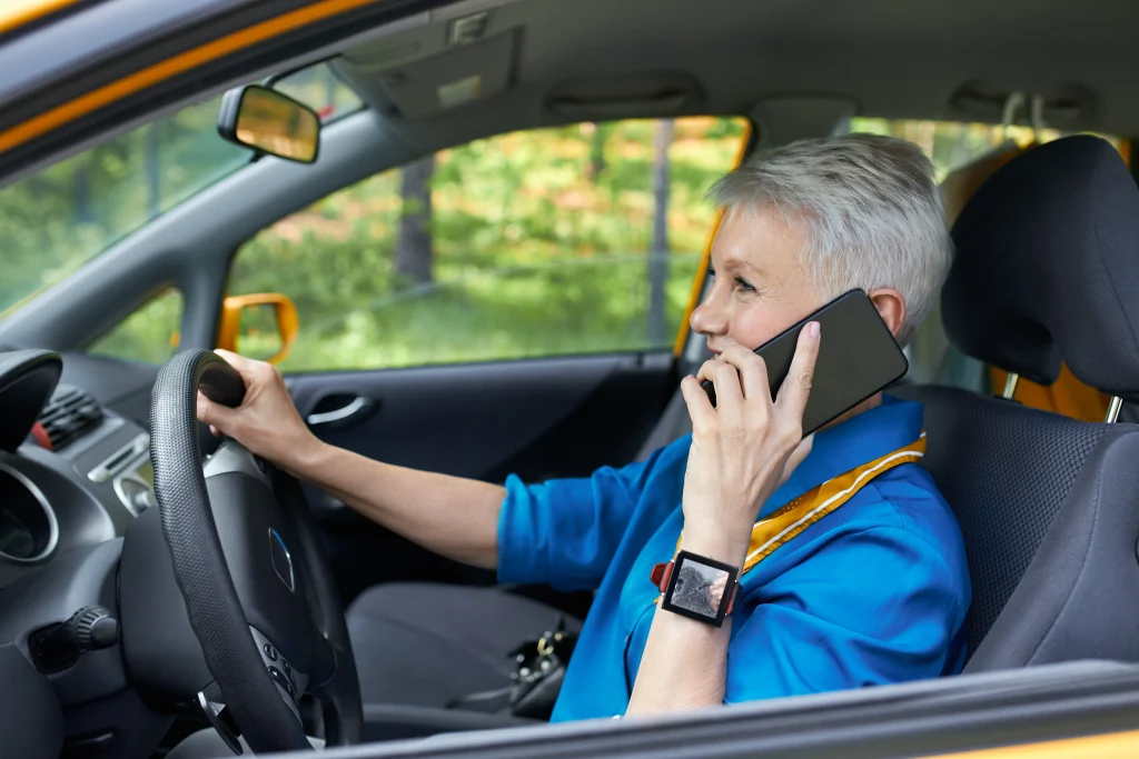 side view fashionable mature careless european female with blonde pixie hair sitting driver s seat with one hand steering wheel holding cell phone talking concentrating road 1